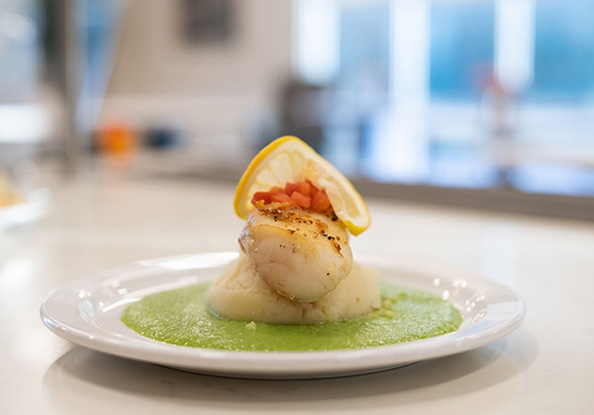 Plate of fish with lemon on creamy green sauce.